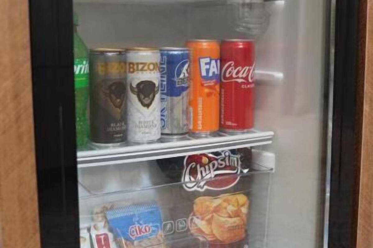 A refrigerator with a shelf of beverages including Coca-Cola, Fanta, and other drinks, and a lower shelf with snacks like chips and a bag of Tacos.