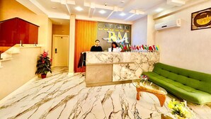 A hotel reception area with a marble floor, a green sofa, and a reception desk with flags.