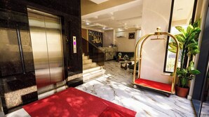 A hotel lobby with a marble floor, a red carpet, a reception desk, and a staircase.