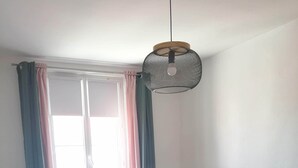 A bedroom with a bed, a window with curtains, a bedside lamp, and a vase with dried flowers. - Maison de Ville à Laleu - La Rochelle (La Rochelle)