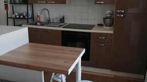A modern kitchen with wooden cabinets, a black stove, a sink, and a white countertop. - Maison de Ville à Laleu - La Rochelle (La Rochelle)