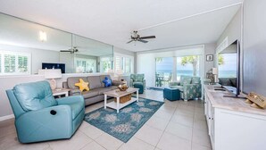 A spacious living room with a sofa, armchair, and coffee table, a large mirror, and a view of the ocean.