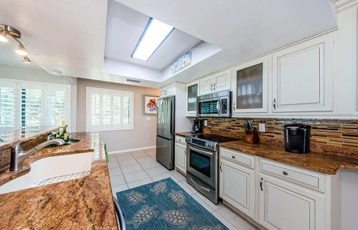 A modern kitchen with white cabinets, stainless steel appliances, and a large window.