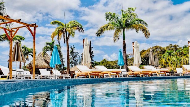 A poolside area with lounge chairs and umbrellas, surrounded by palm trees. - O'Filao (Grand-Bourg)
