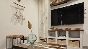 A living room with a wooden coffee table, a wall-mounted TV, and storage boxes labeled 'BAZAR' and 'STORAGE'. - O'Filao (Grand-Bourg)