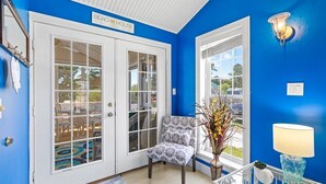 Una habitación con pared azul, un letrero que dice 'BEACH HOUSE', una silla, una lámpara y una ventana con vistas.