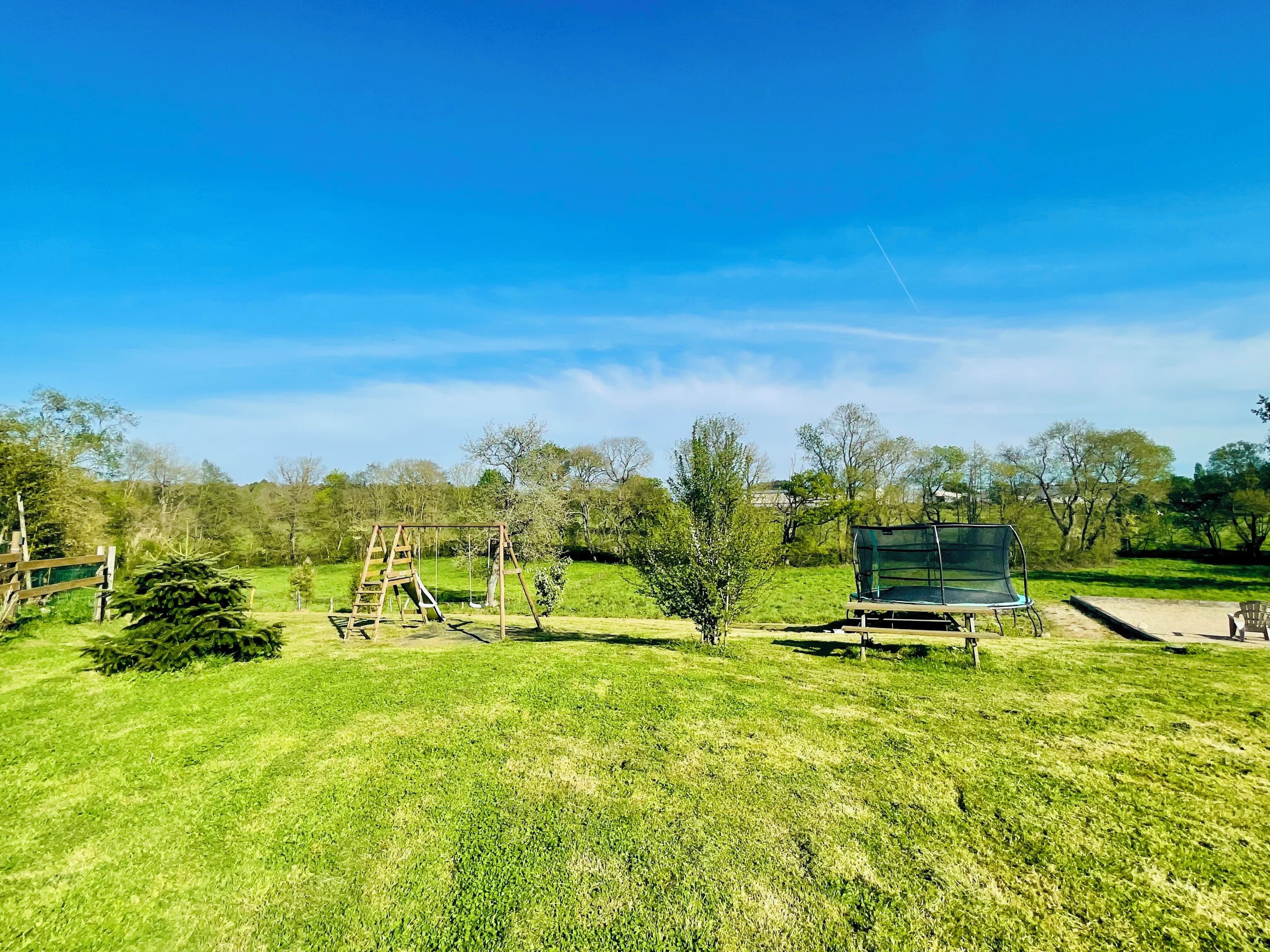 A grassy outdoor area with a swing set, a covered seating area, and trees in the background.