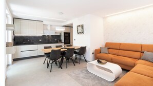 Eine moderne Küche mit weißen Schränken, einer Marmorarbeitsplatte und einem Essbereich mit einem Holztisch und schwarzen Stühlen.