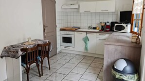 Una cucina compatta con mobili bianchi, un forno a microonde, un fornello e un lavandino. C'è un tavolo da pranzo con sedie e un cestino per i rifiuti.