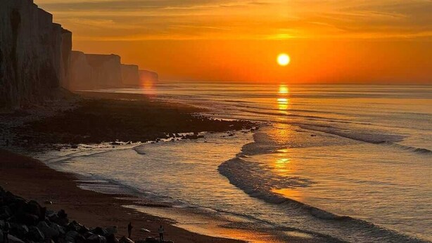 Tramonto su un paesaggio costiero con scogliere e una spiaggia.