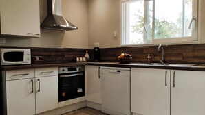 A modern kitchen with white cabinets, a microwave, an oven, a dishwasher, and a window with a view of trees. - Nouveau Maison Avec Jardin aux Portes des Gorges de L'ardèche (Saint-Julien-de-Peyrolas)