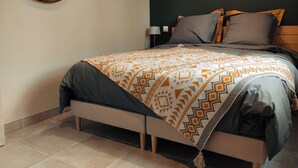 A neatly made bed with patterned bedding, a wall-mounted mirror, a framed picture, and a bedside table with a lamp. - Nouveau Maison Avec Jardin aux Portes des Gorges de L'ardèche (Saint-Julien-de-Peyrolas)