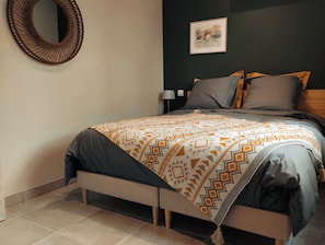 A neatly made bed with patterned bedding, a wall-mounted mirror, a framed picture, and a bedside table with a lamp.