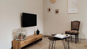 A living room with a TV mounted on the wall, a wooden console table with a glass terrarium, a chair with patterned upholstery, and a framed map on the wall. - Nouveau Maison Avec Jardin aux Portes des Gorges de L'ardèche (Saint-Julien-de-Peyrolas)