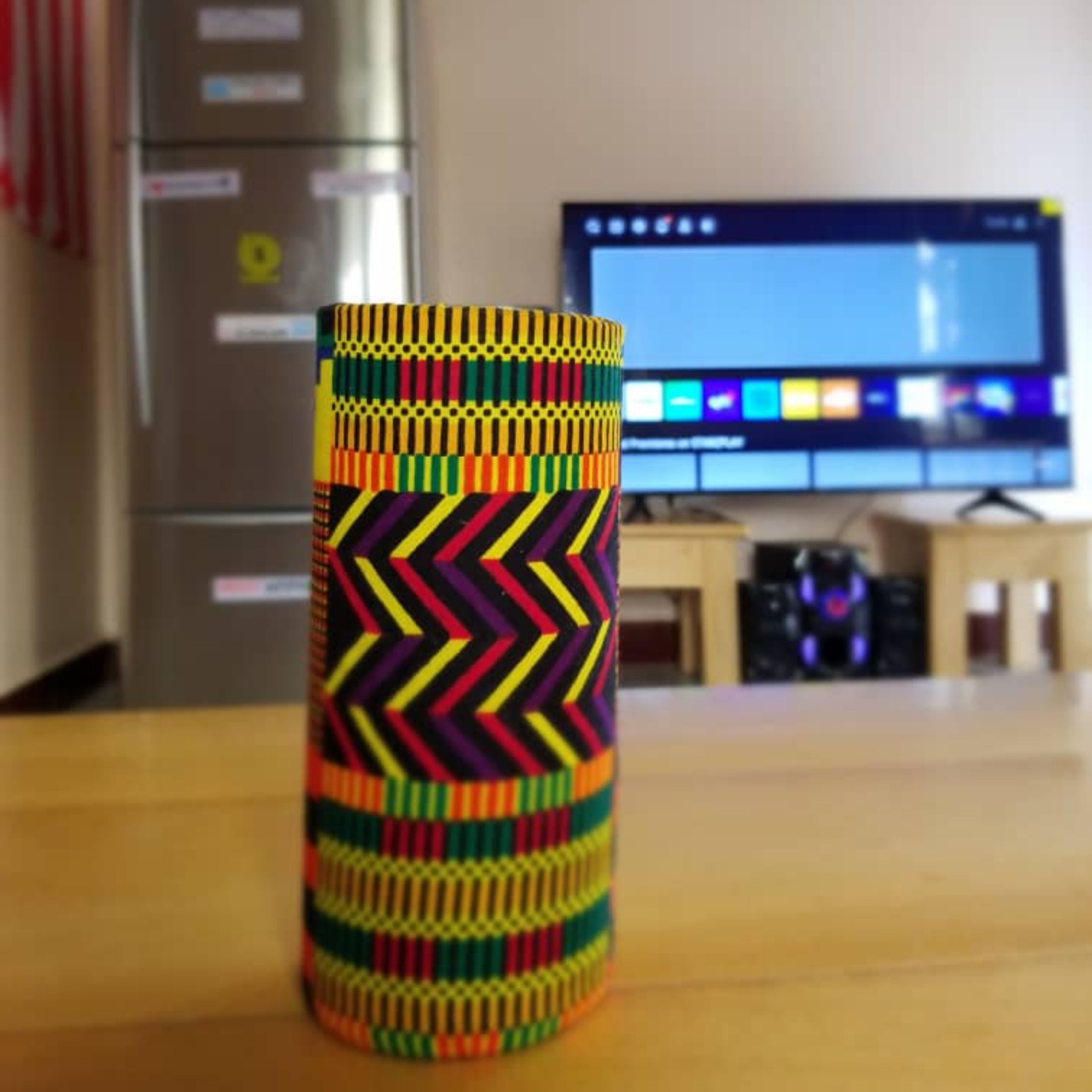 Un objeto cilíndrico y colorido sobre una mesa, con un monitor de computadora al fondo.