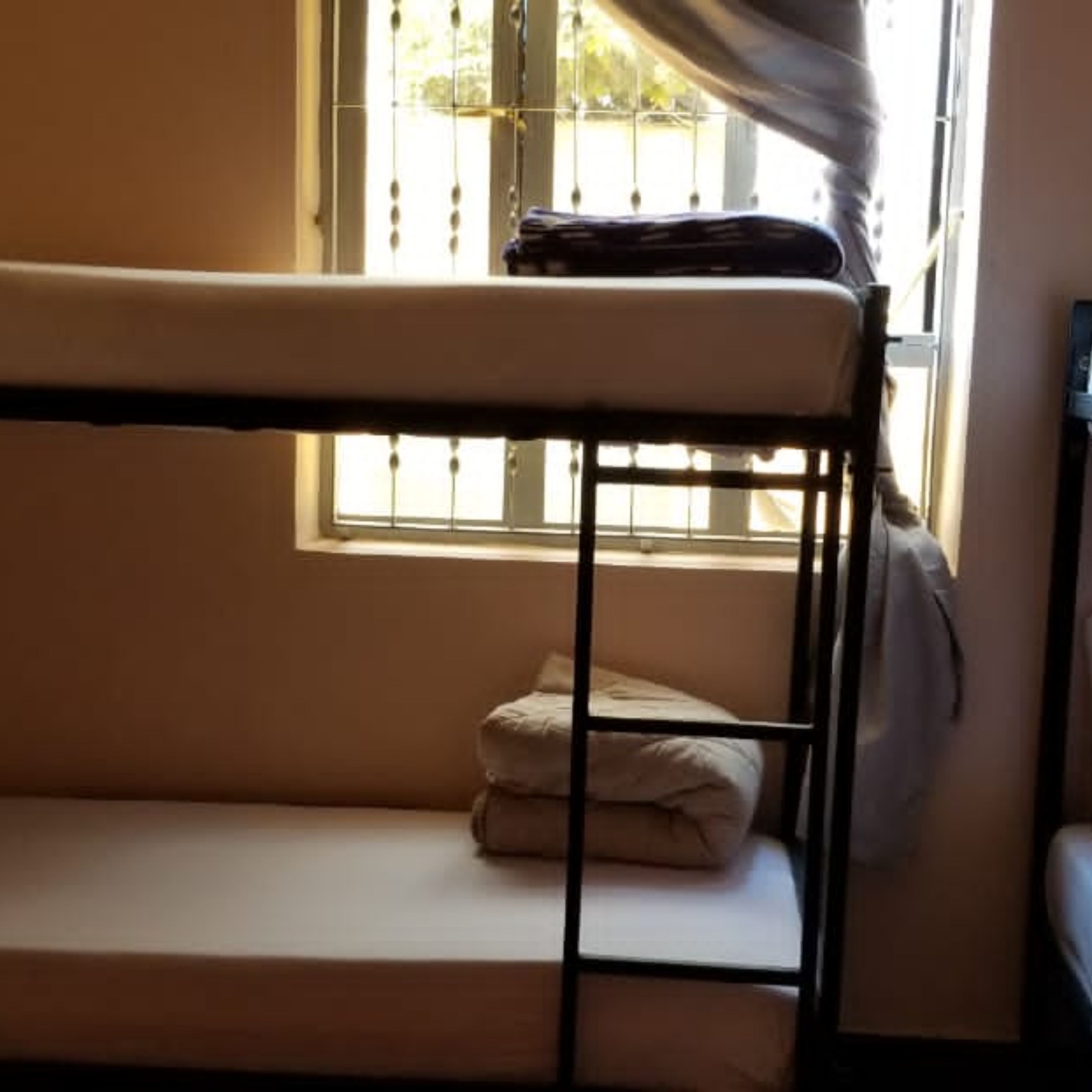 A bunk bed with a mattress and pillows, a window with curtains, and a chair.