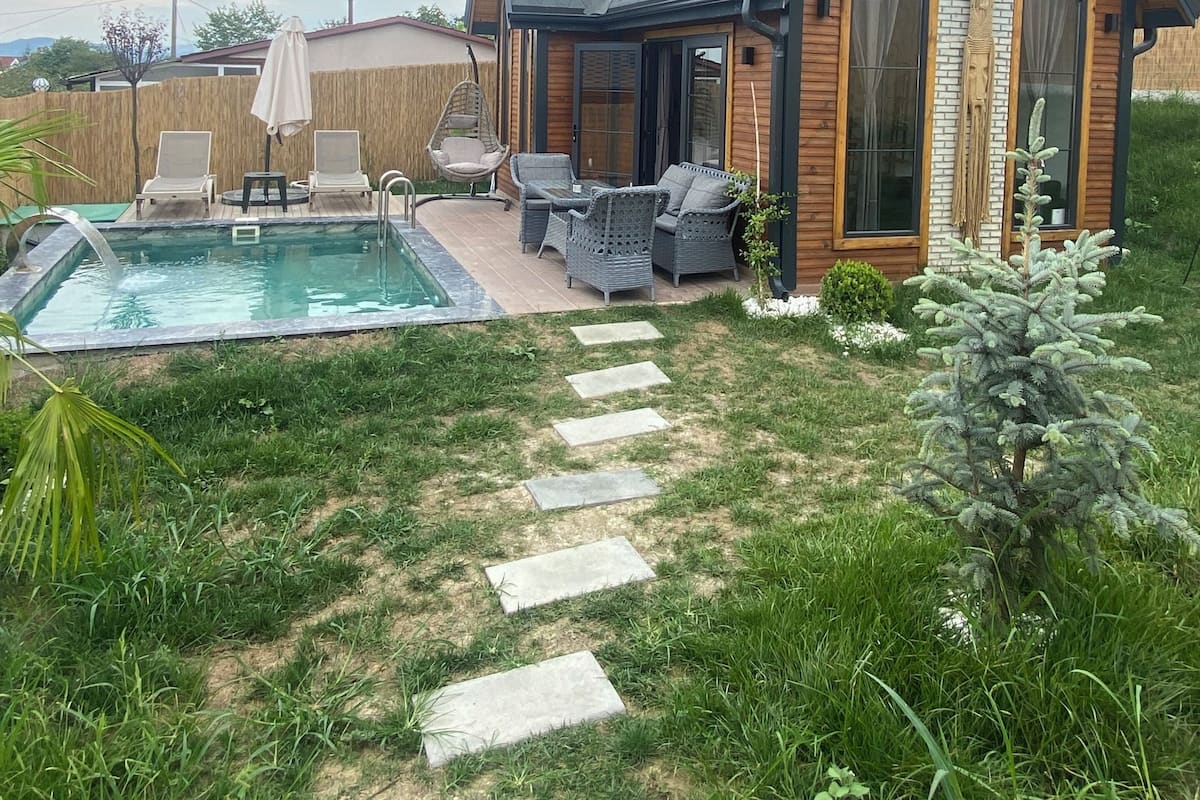 A modern house with a swimming pool, outdoor seating, and a stone pathway leading to the entrance.