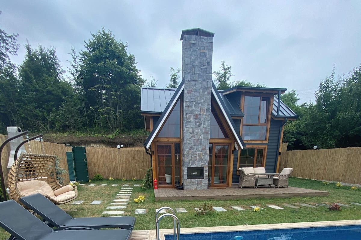 A modern house with a stone chimney, a swimming pool, and outdoor furniture.