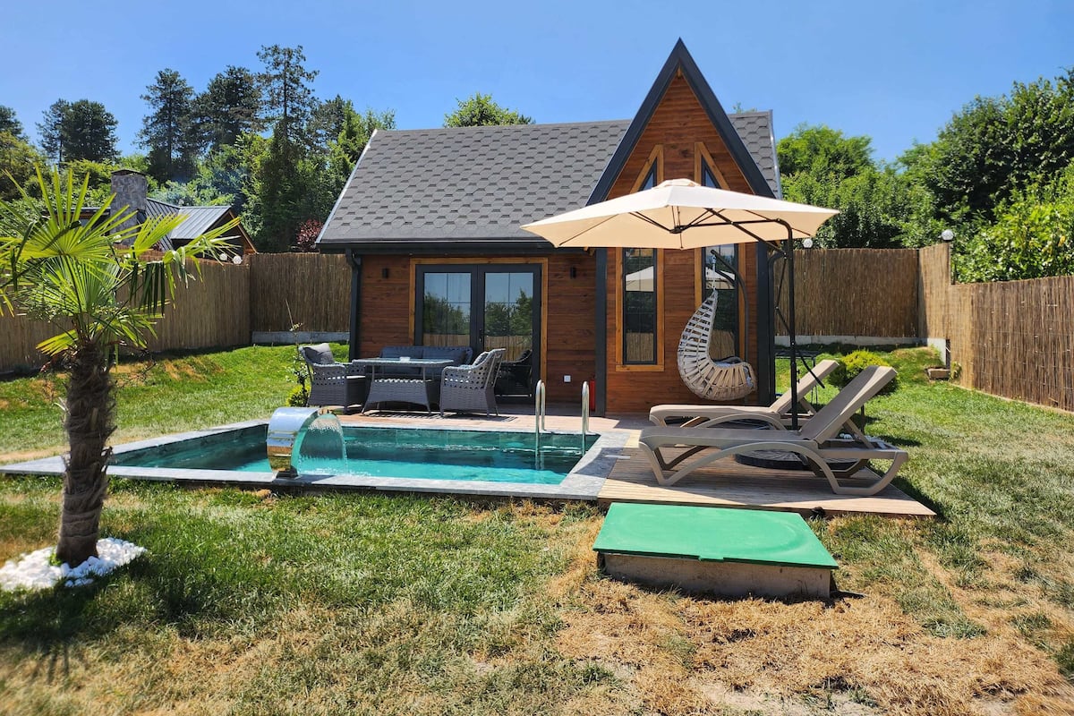A backyard with a swimming pool, outdoor furniture, and a wooden house.