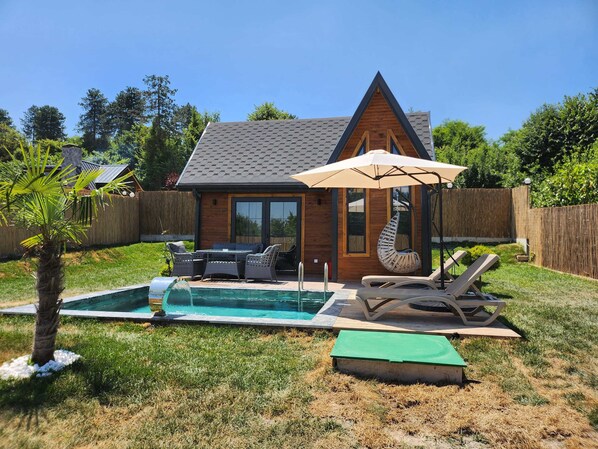 Un jardin avec une piscine, du mobilier d’extérieur et une maison en bois.