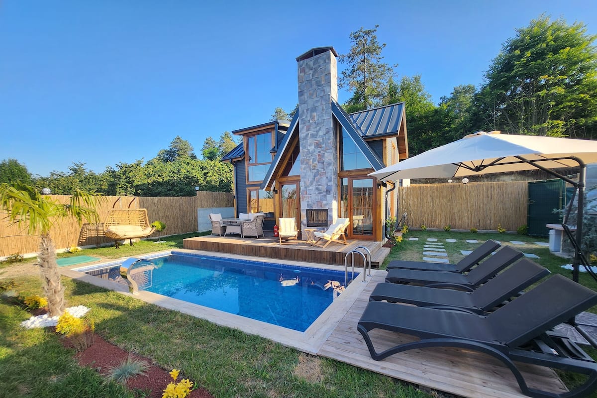 A modern house with a stone chimney, a swimming pool, and outdoor seating.