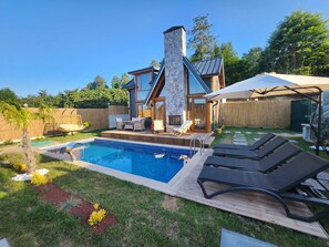 Une maison moderne avec une cheminée en pierre, une piscine et un espace salon extérieur.