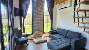 A modern living room with a wooden ceiling, a stone fireplace, and a large gray sectional sofa. - Mayan Bungalows (Sapanca)