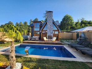 Une maison moderne dotée d’une cheminée en pierre, d’une piscine et de mobilier d’extérieur.