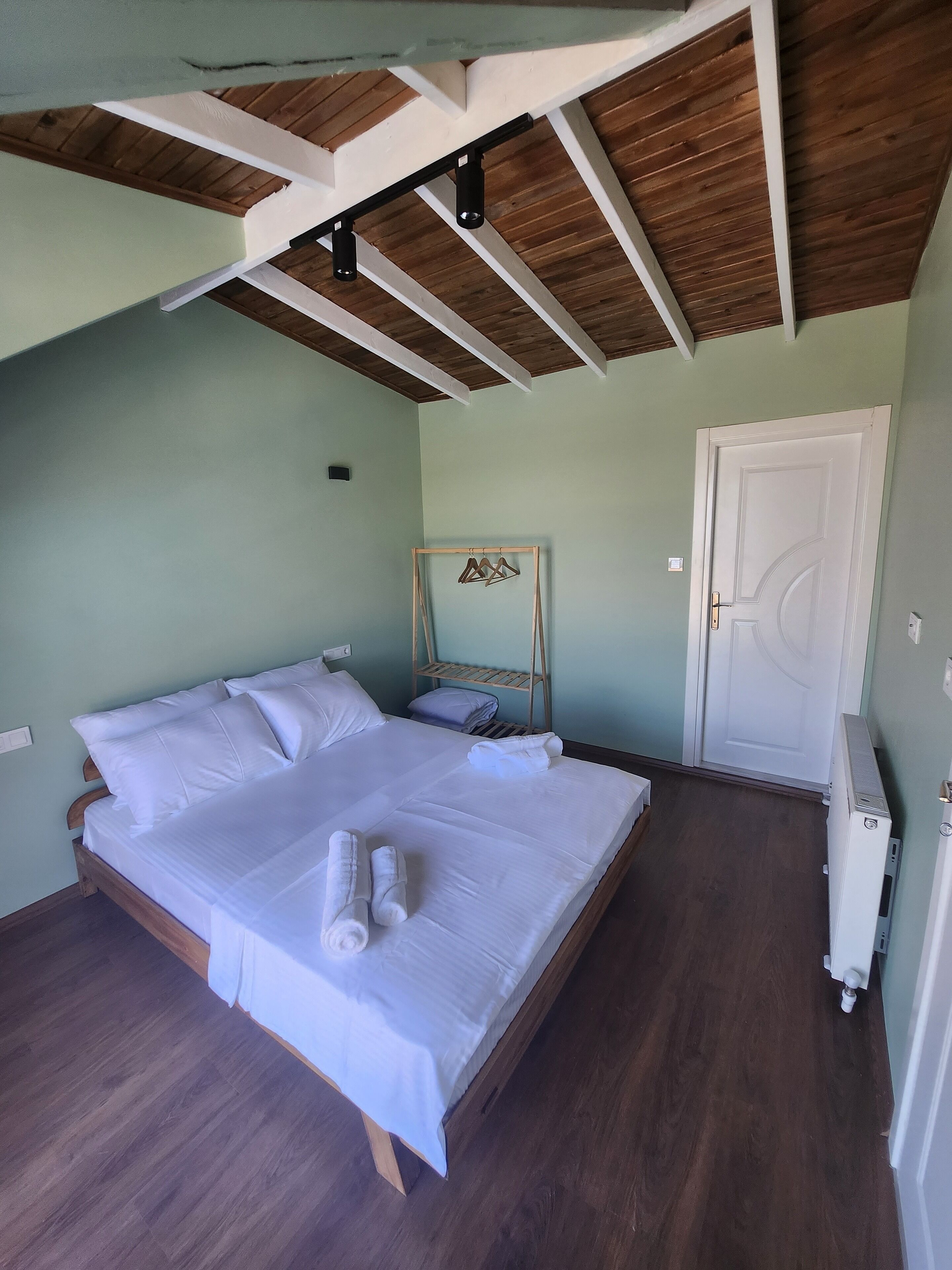 Une chambre à coucher avec un lit en bois, du linge de lit blanc, une tête de lit en bois, une porte blanche et un radiateur.