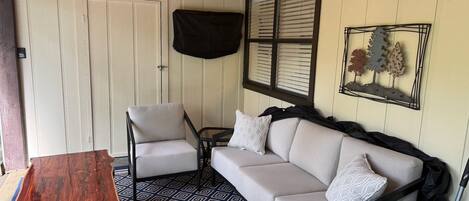 Une pièce chaleureuse avec un plafond en bois, un ventilateur de plafond, une porte blanche, une chaise noire, un canapé beige et un tapis à motifs.
