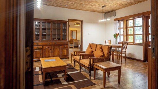 Amplia sala de estar con muebles de madera, una mesa de comedor y vistas al exterior a través de grandes ventanales.