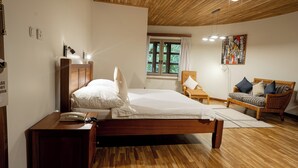 Un dormitorio con una cama de madera, una mesita de noche con un teléfono, una ventana con cortinas y un sillón de mimbre con cojines.