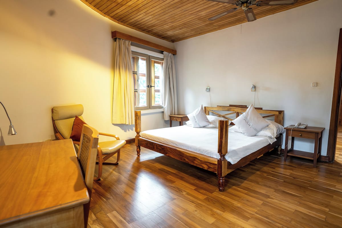 Un dormitorio con una cama de madera, una silla, un escritorio y una ventana con cortinas.