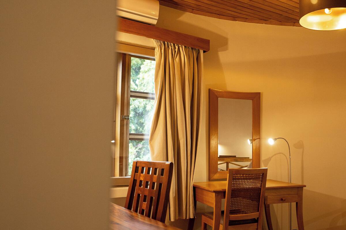 Una habitación con un escritorio de madera, dos sillas, un espejo y un ventanal con cortinas.