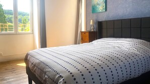 Un dormitorio con cama, mesita de noche, lámpara, ventana con cortinas y un cuadro en la pared.