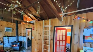 Interior acogedor de una cabaña con chimenea, paredes de madera, una puerta roja y una escalera.