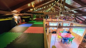 Habitación en ático con coloridos tapetes de espuma, vigas de madera, una mesa con sillas y luces de cuerda.