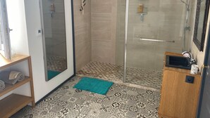 Ein Badezimmer mit Duschkabine aus Glas, einem hölzernen Ablagebrett mit Handtüchern und fliesenbesetztem Boden.