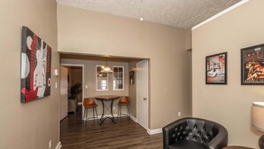 A hallway with a dining area, a black leather chair, and a lamp.