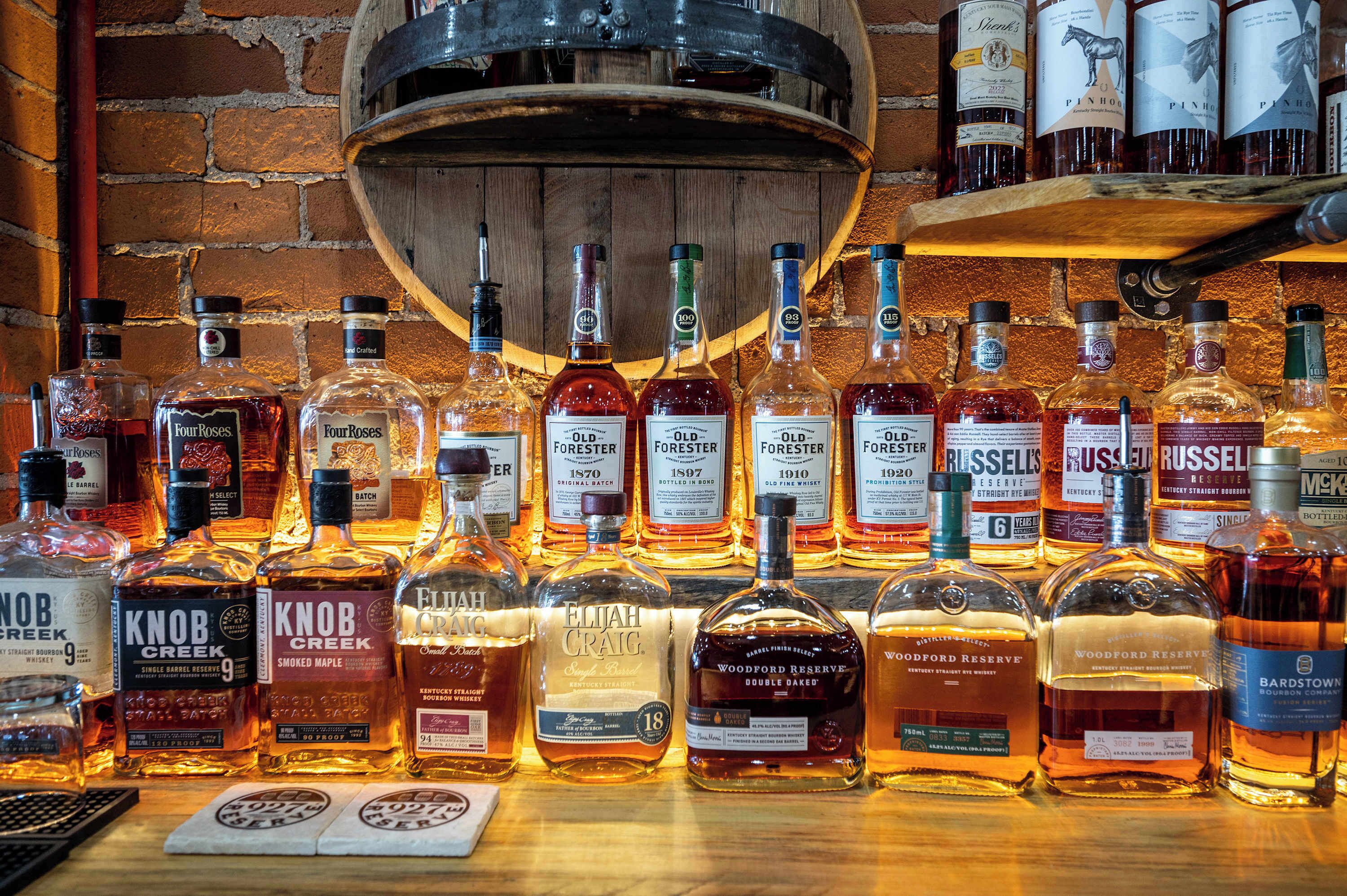 A variety of whiskey bottles displayed on a wooden surface with a brick wall background.