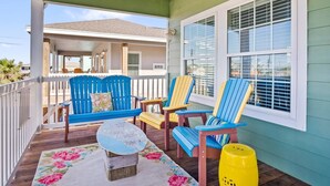 A covered porch with a wooden deck, a blue and yellow Adirondack chair, a wooden bench, and a small table with a floral table runner.