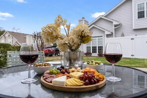 Une table en verre sur laquelle sont disposés un plateau de fromages, des raisins, des noix et deux verres de vin rouge.