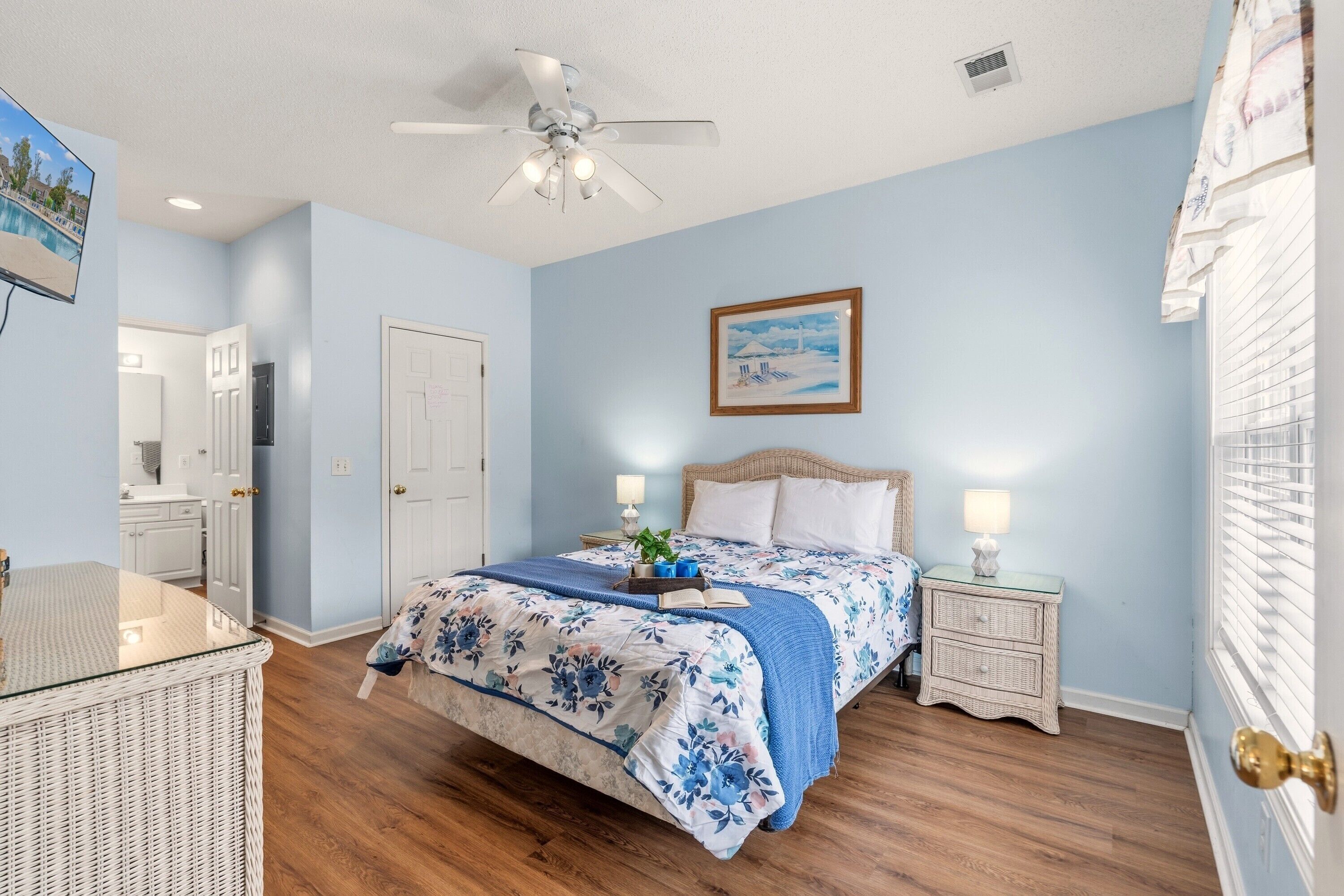A bedroom with a bed, bedside tables, a ceiling fan, and a painting on the wall.
