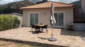 Eine Terrasse mit Tisch und Stühlen, einem Sonnenschirm und Blick auf Berge im Hintergrund.