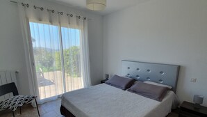 Ein Schlafzimmer mit einem Bett, einem Sessel, einem Nachttisch und einem Fenster mit Vorhängen.