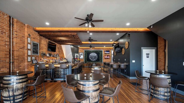 A bar area with wooden barrels as tables, metal chairs, and a counter with various bottles. - Monmouth Lofts (Newport)