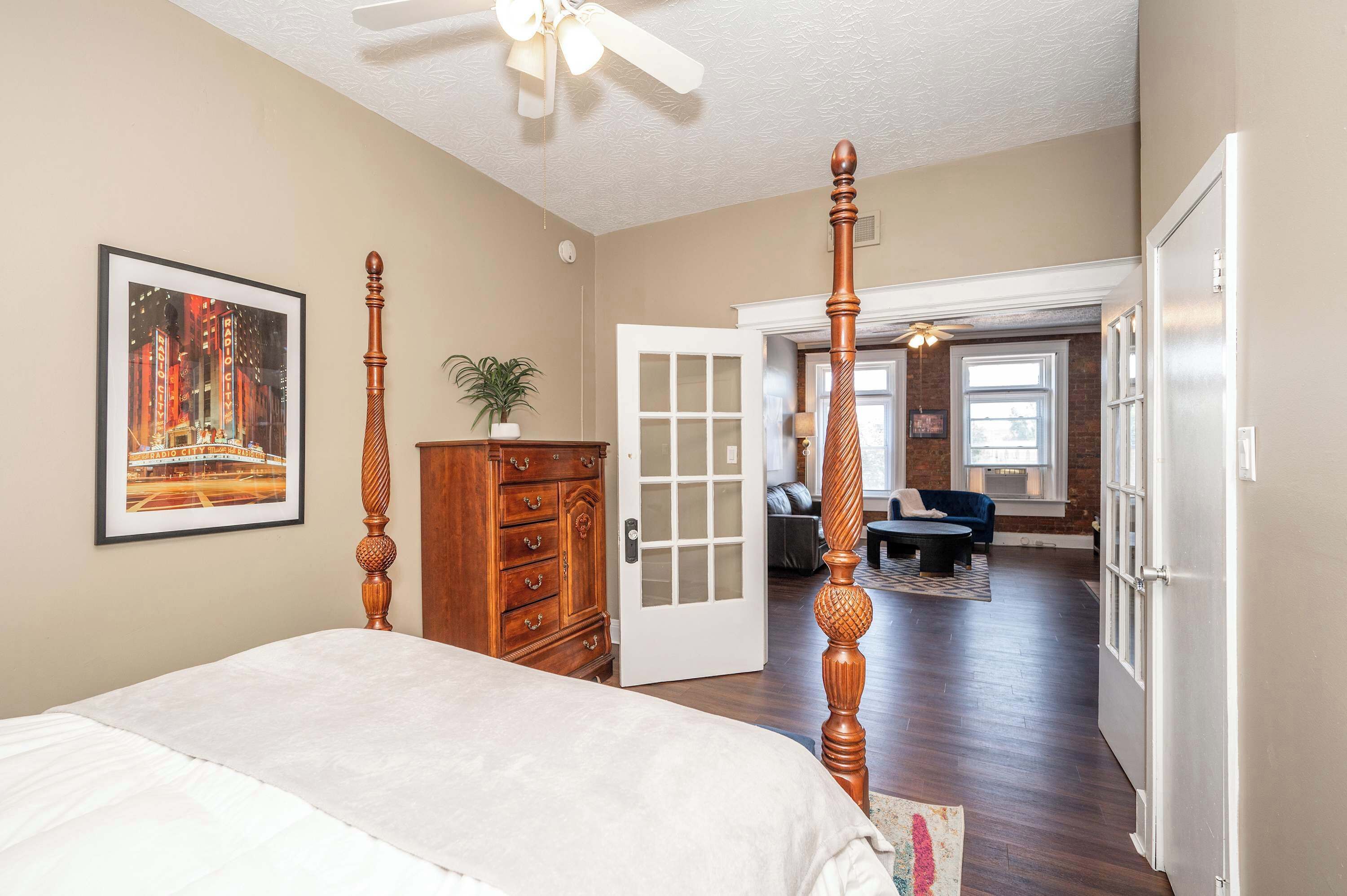 A bedroom with a four-poster bed, a dresser, and a door leading to another room.