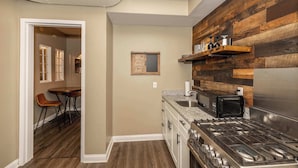 A kitchen with a wooden backsplash, a gas stove, a microwave, and a dining area with a table and chairs. - Monmouth Lofts (Newport)