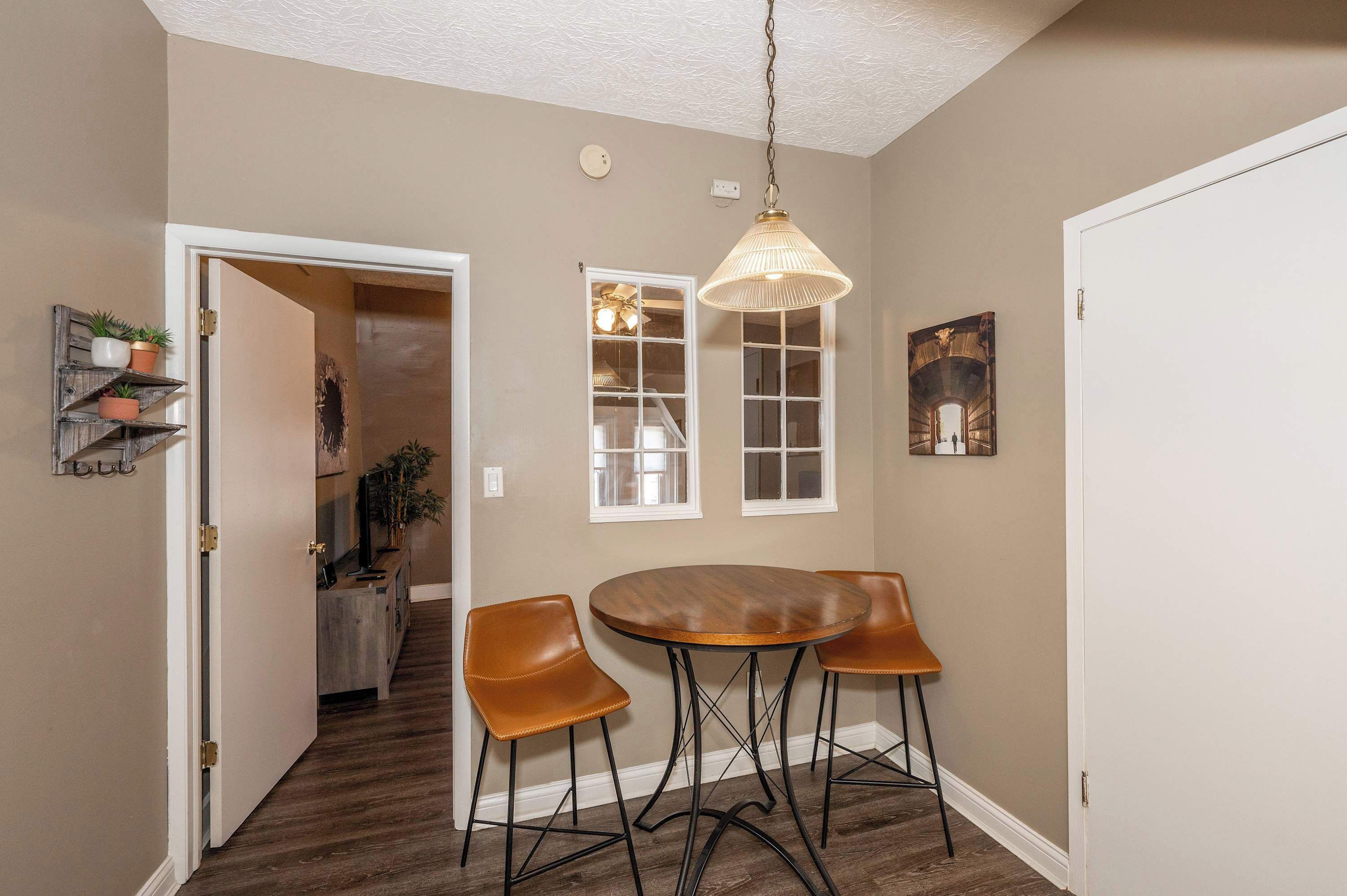A dining area with a round table and two chairs, a pendant light, and a view into a hallway with a door and a staircase.