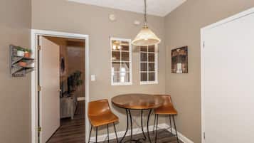 A dining area with a round table and two chairs, a pendant light, and a view into a hallway with a door and a staircase.